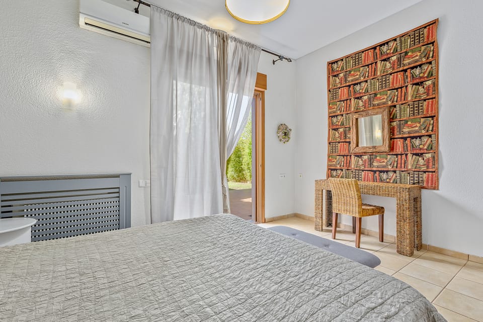A Charis bedroom with a wicker desk and glass door to the garden