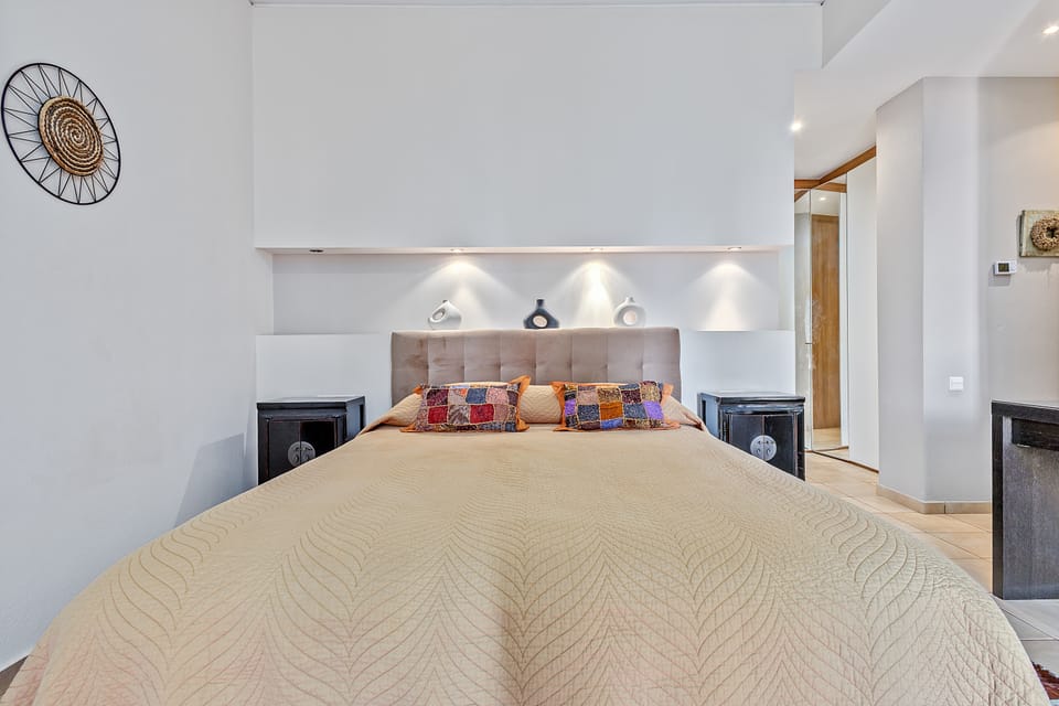 A Charis bedroom with a quilted bedspread, upholstered headboard, and an illuminated display niche