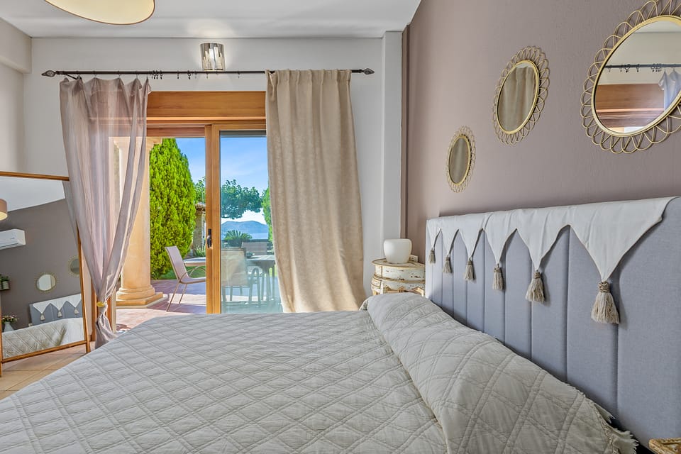 A Charis bedroom with round gold mirrors opening through sliding doors to the sea-view terrace