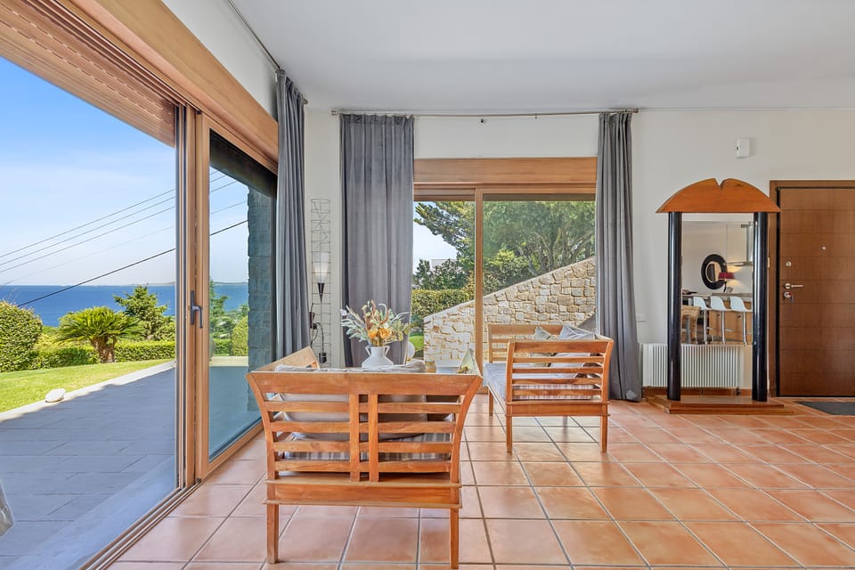 A Charis living area with wooden chairs and floor-to-ceiling glass doors to the garden and sea