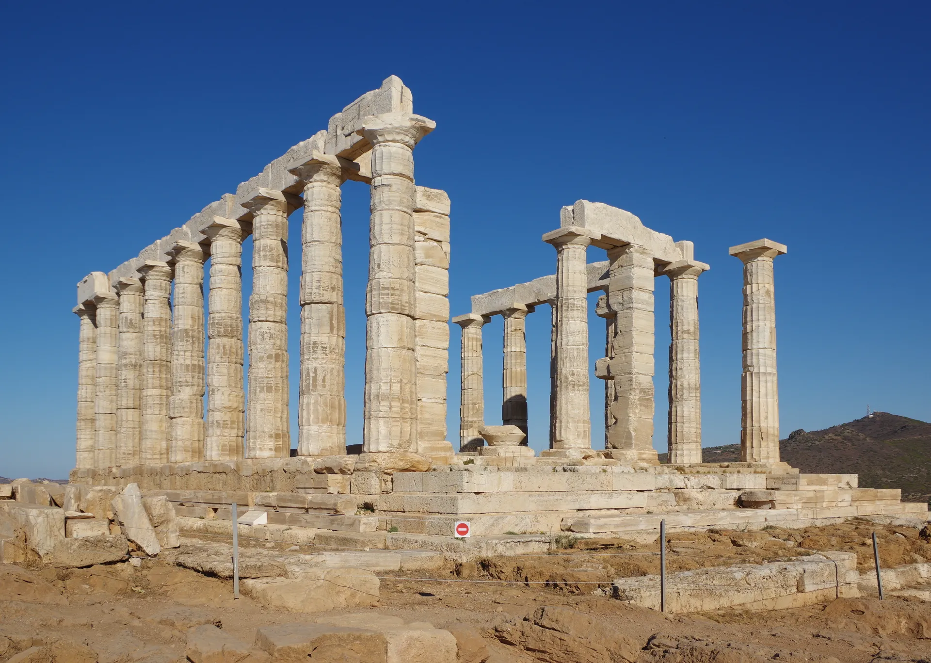 The corner colonnade of the Temple of Poseidon in midday sun, hills behind
