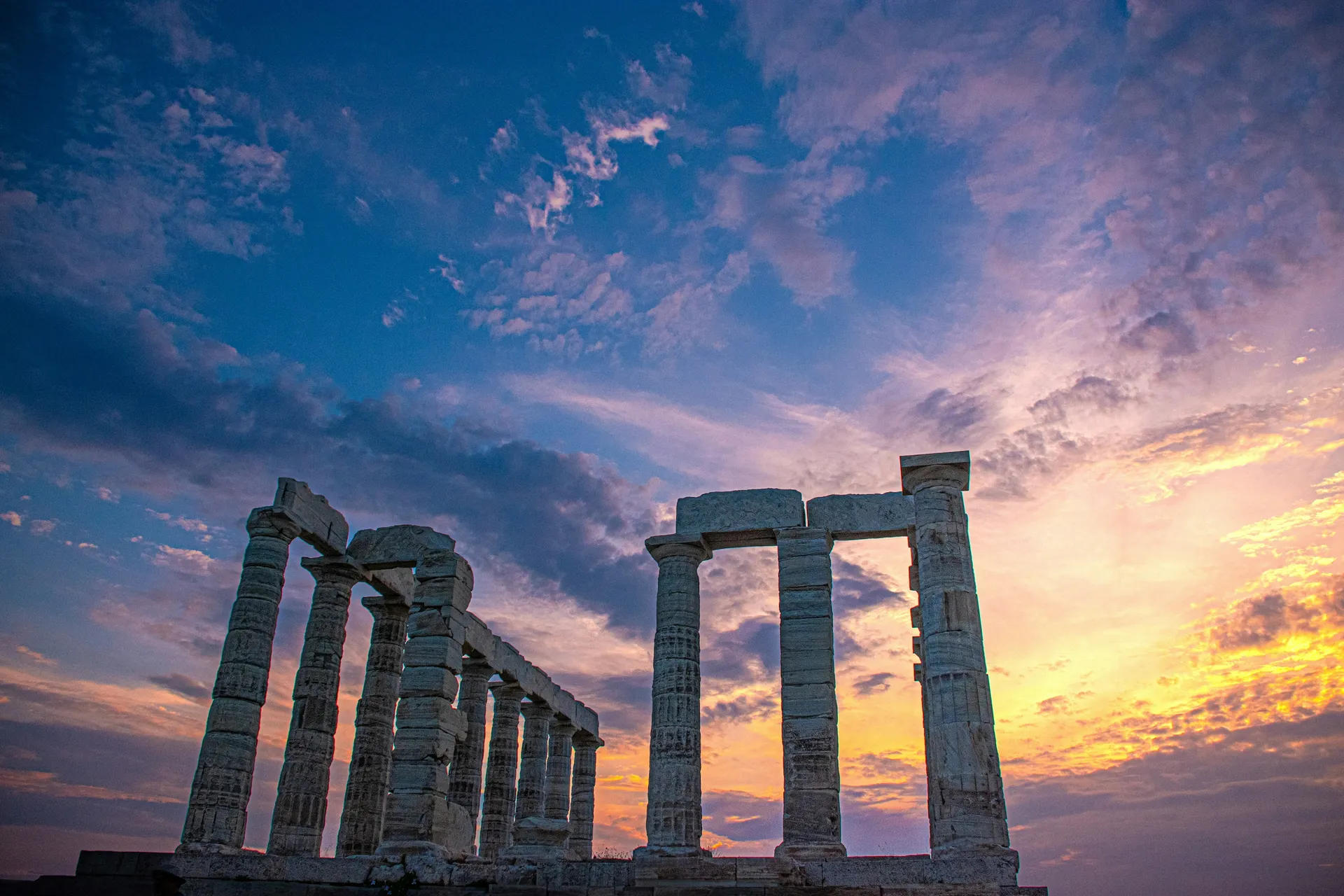 The columns of the Temple of Poseidon against a golden sunset sky