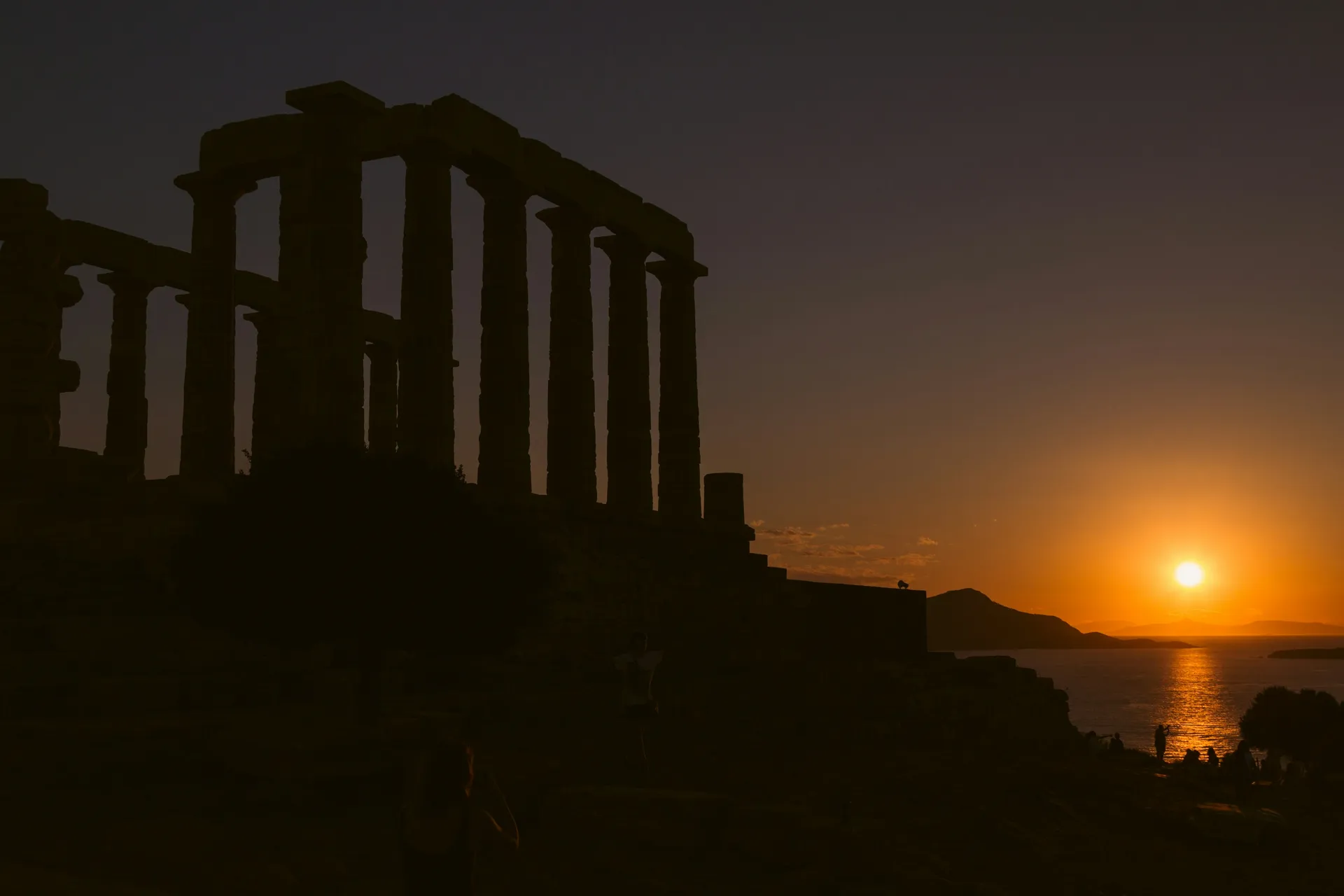 The Temple of Poseidon at Cape Sounion silhouetted against the setting sun over the sea